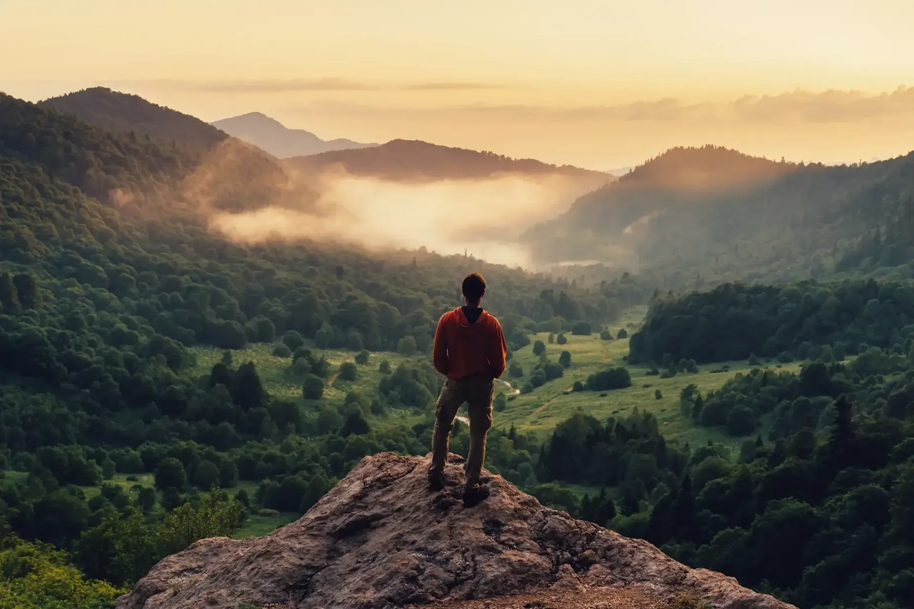 Wanderer auf einem Felsvorsprung über einem nebligen Bergtal im Morgenlicht