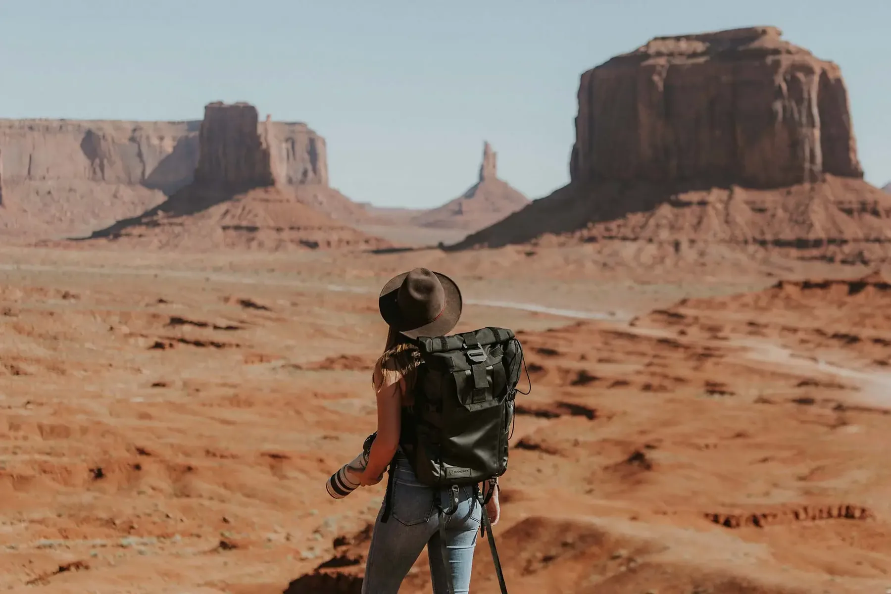 Reisende mit Rucksack und Hut blickt über die roten Tafelberge des Monument Valley